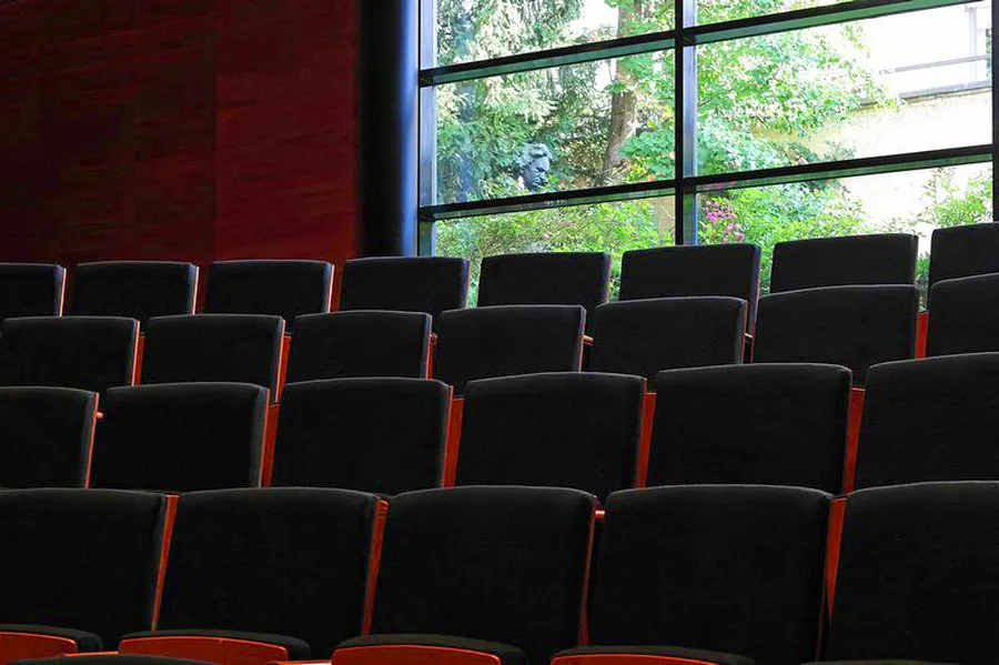 Rows of chairs with black seat cushions, behind them the window of the chamber music hall with a view of the museum garden.